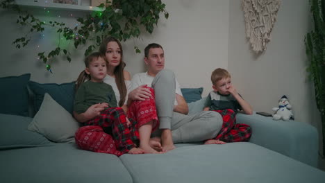 Family-of-three---father-mother-and-tow-son-watching-TV-in-the-evening.-Togetherness-quarantine-stay-home.-High-quality-4k-footage